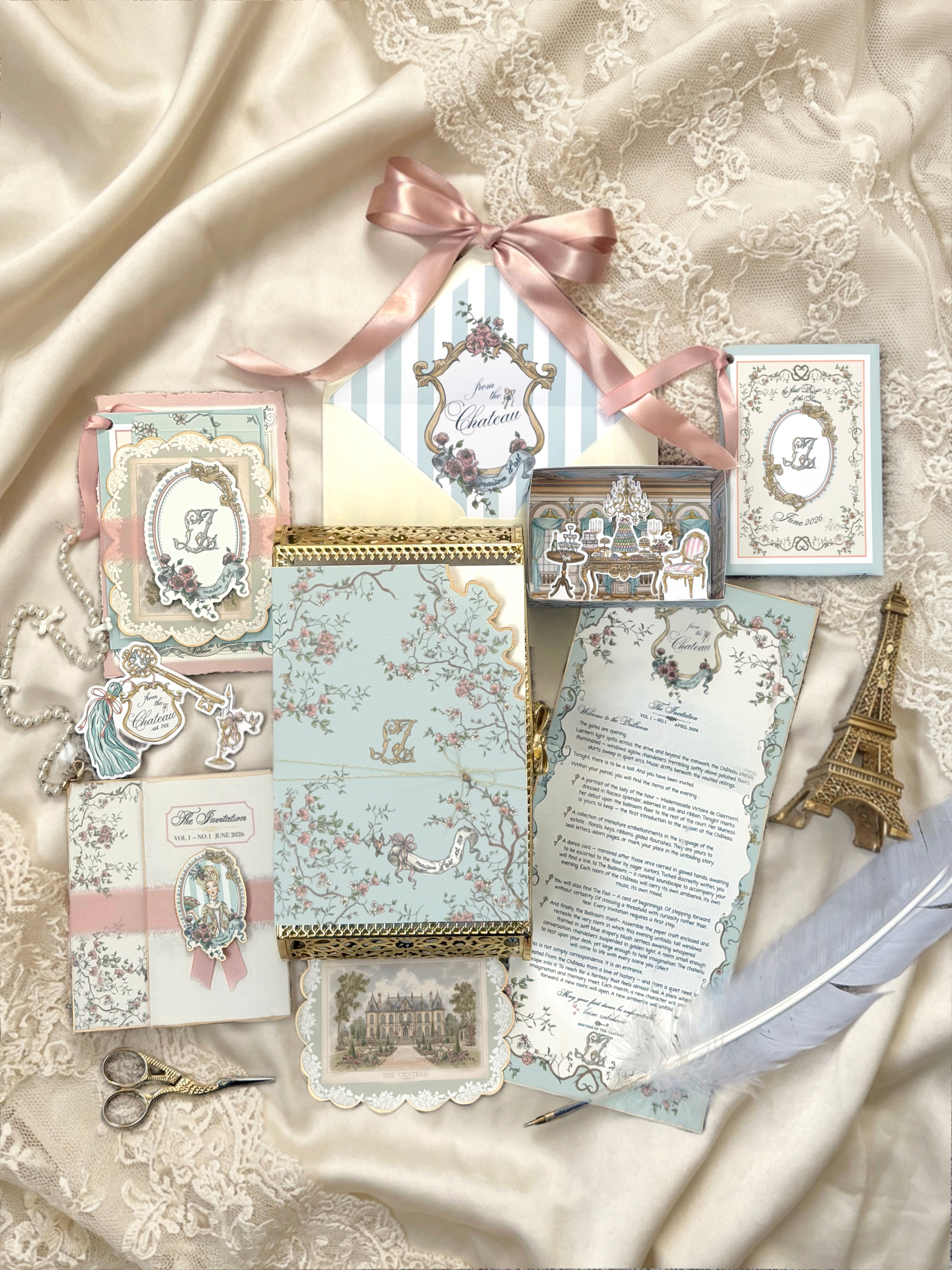 From the Chateau Mail Club collection featuring a monthly letter, château-inspired paper goods, miniature room craft, artwork, tags, and stationery arranged on ivory satin
